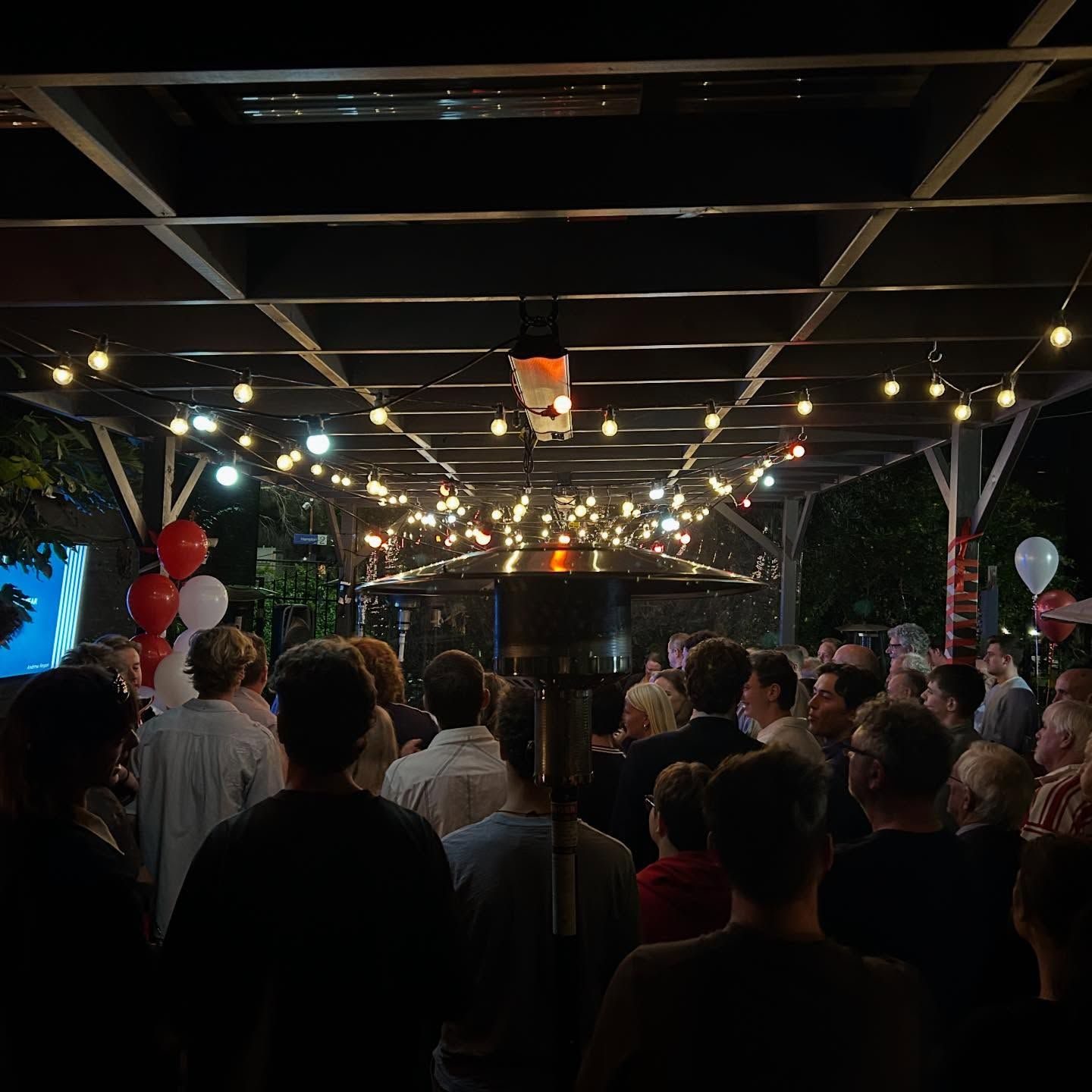 A full beer garden at night under strings of lights